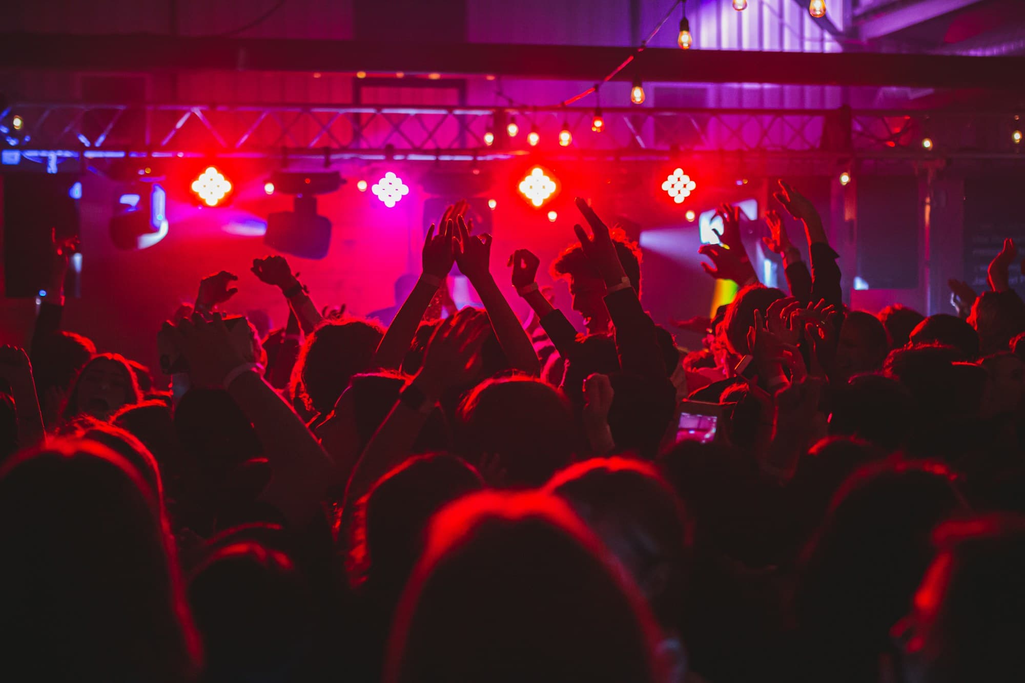Club night crowd with hands up under truss-mounted red LED fixtures
