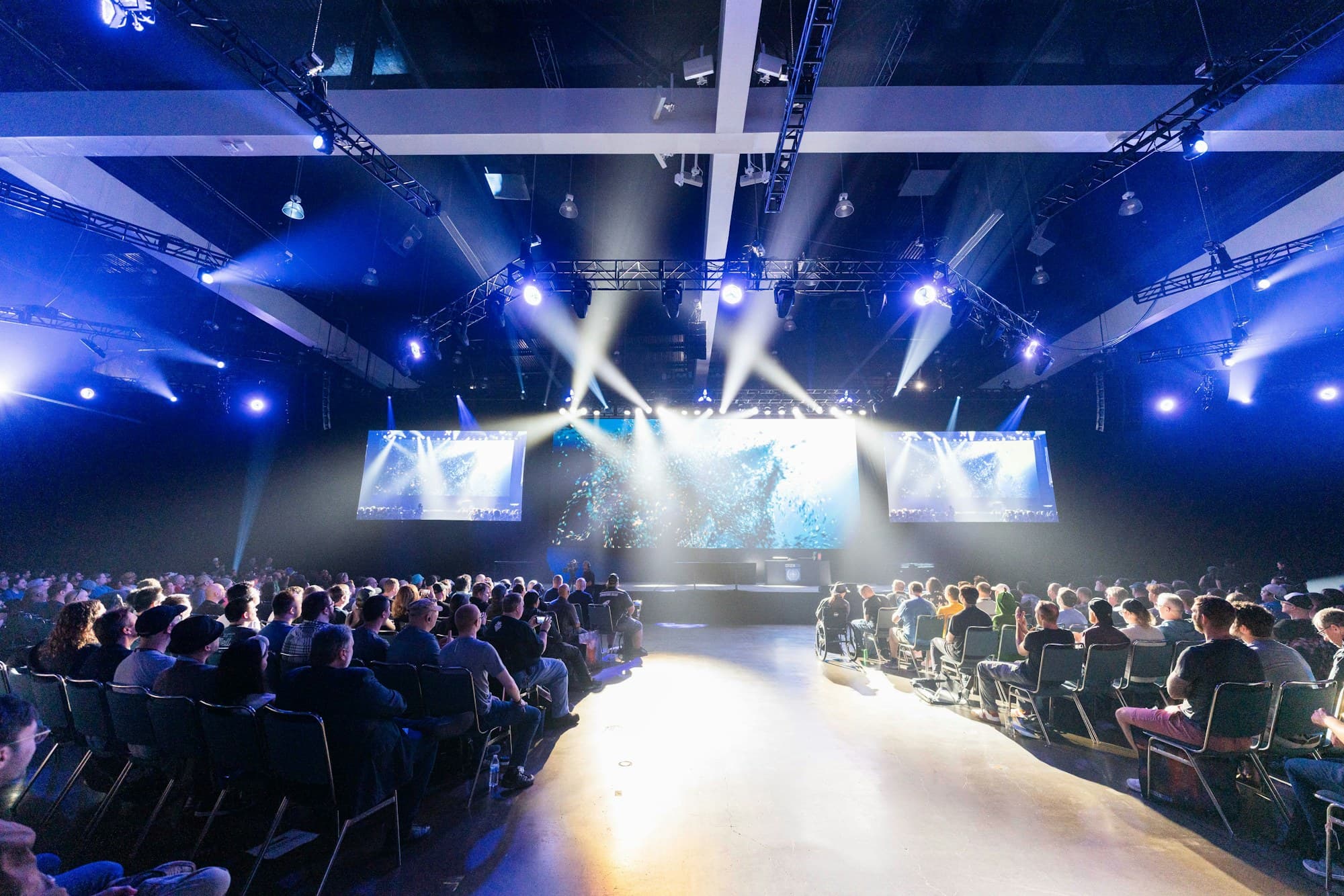 Corporate conference hall with truss-mounted moving heads, LED screens and a seated audience