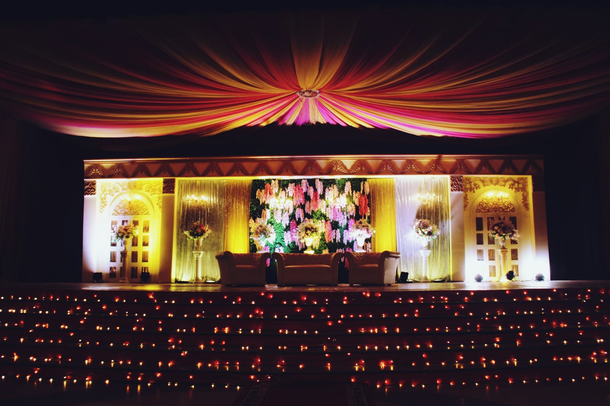 Wedding reception stage with draped ceiling, floral backdrop and warm stage lighting